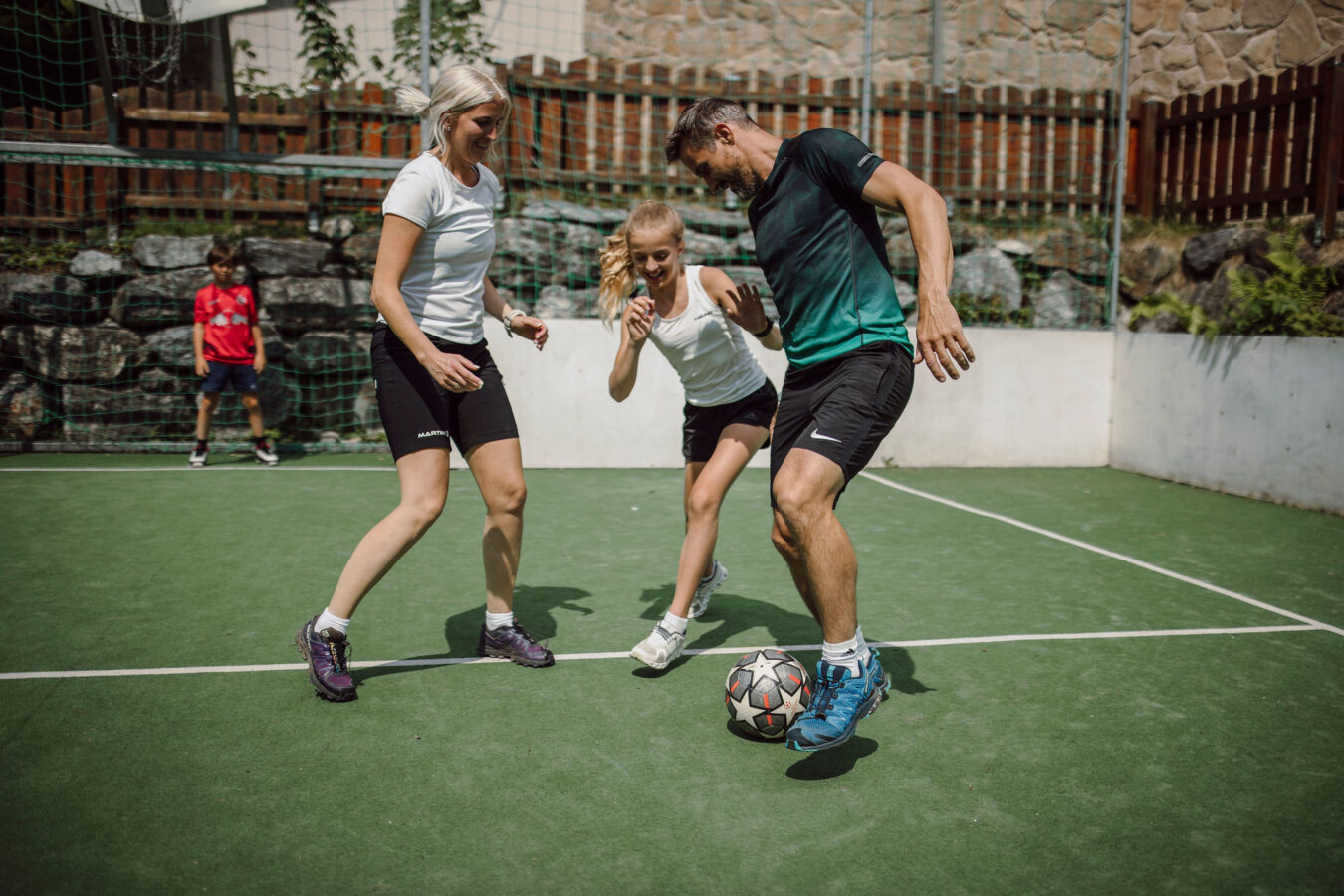 Eine Familie spielt Fussball am Fussballplatz vor dem Hotel Alpina Alpendorf.