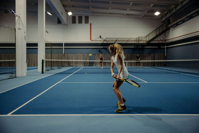 In der Tennishalle vom Hotel Alpina Alpendorf spielen Teenager gemeinsam mit Trainer.