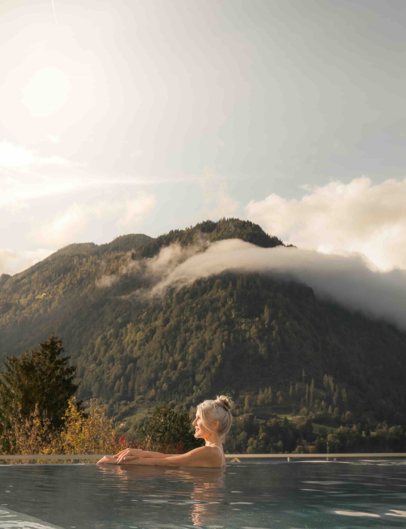 Eine Frau schwimmt im beheizten outdoor Pool vom Hotel Alpina Alpendorf bei herbstlichem Wetter.
