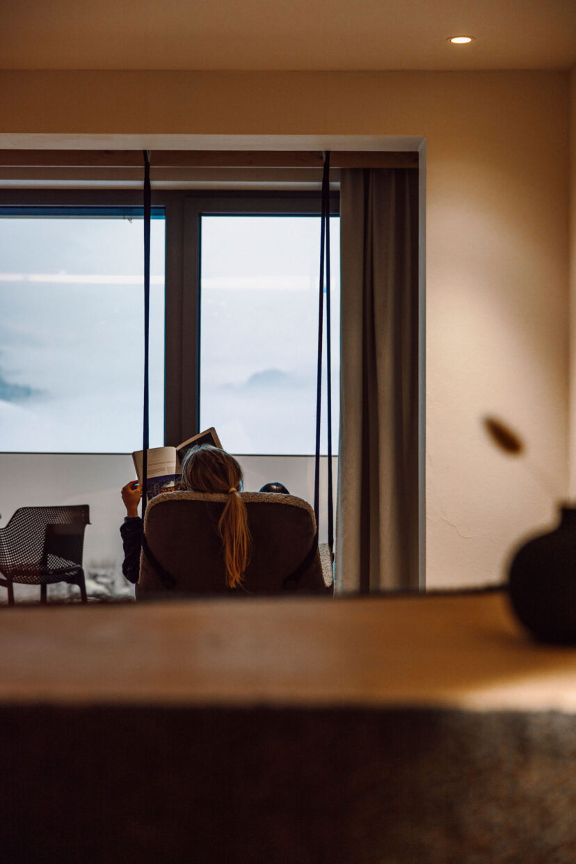Eine Frau genießt die Winterlandschaft in der modernen Suite vom Alpina Alpendorf.
